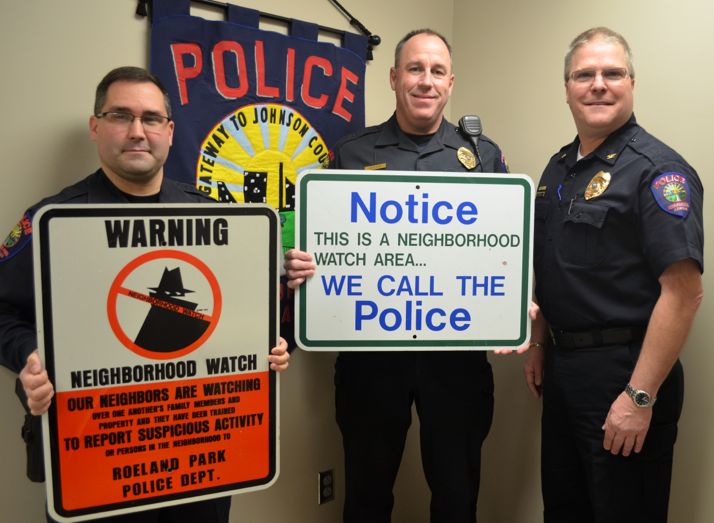 Roeland Park corporals Warren Gardner (L), and Charlie Kotcher and Police Chief John Morris (R) display neighborhood watch signs.