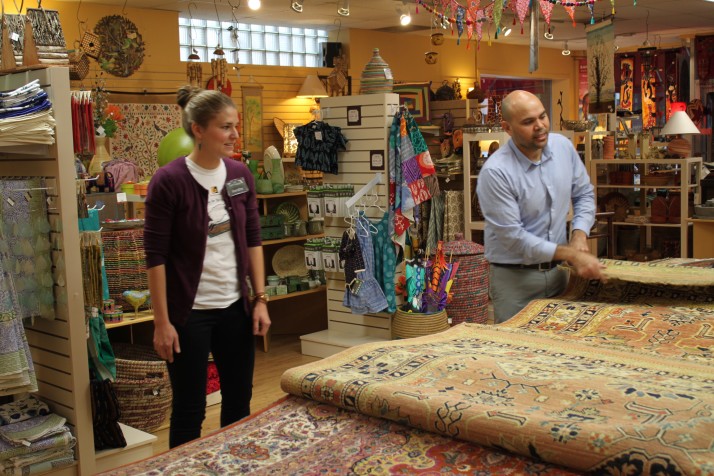 Kendra Frink watches Amir Chaman of the Bunyaad group display hand-made rugs from Pakistan.