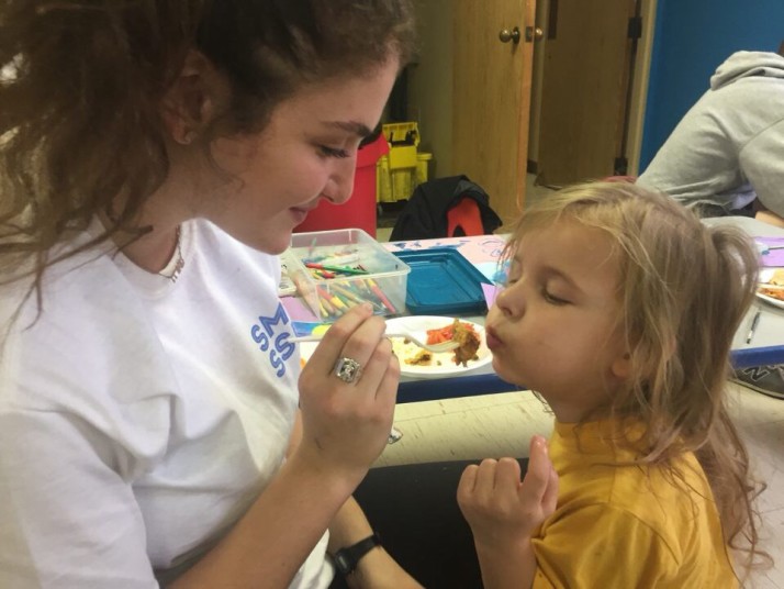 Lauren Cole helps feed a child at Avenue of Life in KCK for her SME Senior Service Day project.