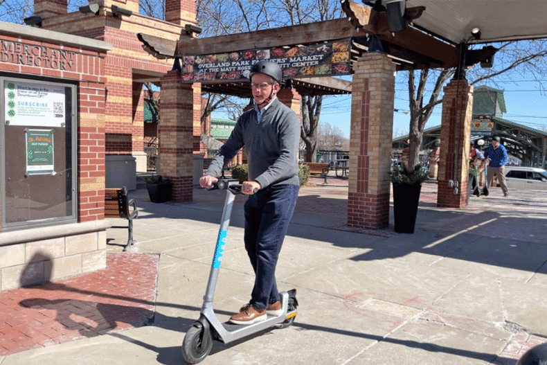 The City of Overland Park has launched a two-year pilot program for Bird electronic rental scooters. The scooters have a maximum speed of 15 miles per hour and can be ridden on bike lanes, sidewalks and some streets within city limits. Above, Mayor Curt Skoog takes a ride across Clock Tower Plaza in downtown Overland Park Tuesday. Photo via City of Overland Park.